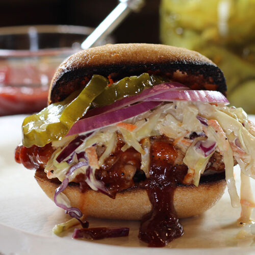 BBQ Chicken Sandwich on a plate with sauce and pickles in background