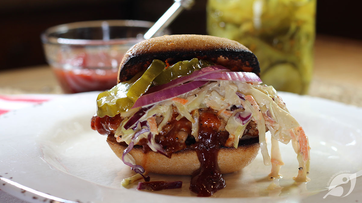 BBQ Chicken Sandwich on a plate with sauce and pickles in background