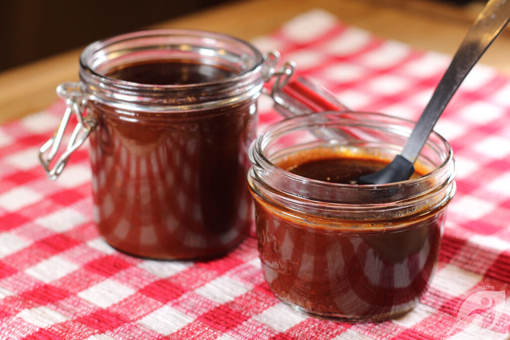 Two canning jars of Homemade BBQ Sauce on a red checker placemat.