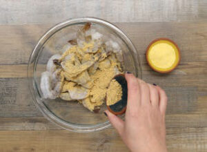 adding cornmeal and Blazin' Buffalo Blend to raw shrimp in a bowl