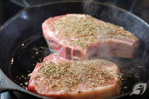 Herbes de Provence seasoned pork chops in a cast iron skillet