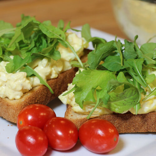 Egg salad spread on toast with baby lettuce and microgreens, served on a plate with grape tomatoes.