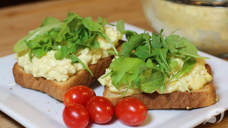 Egg salad spread on toast with baby lettuce and microgreens, served on a plate with grape tomatoes.