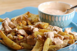 Closeup of fries with a drizzle of our favorite dipping sauce with bowl of sauce in the background.