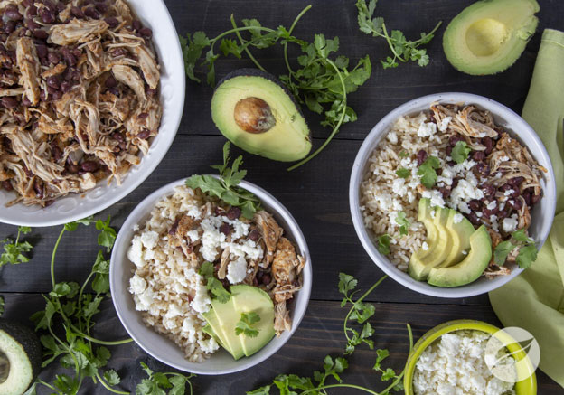 Two Pollo Asada Rice Bowls with shredded chicken in a seperate bowl cheese and avocado on a board