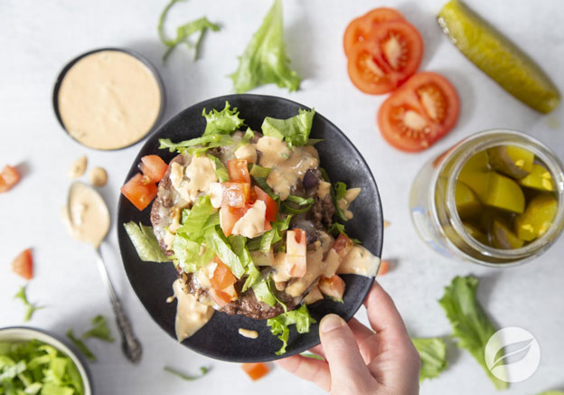 hand holding Burger Bowl with lettuce, tomato, pickle and dressing in background