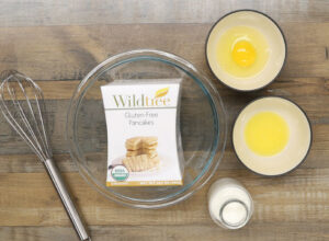 Wildtree Gluten-Free Pancakes Mix package next to bowls with egg, milk and melted butter