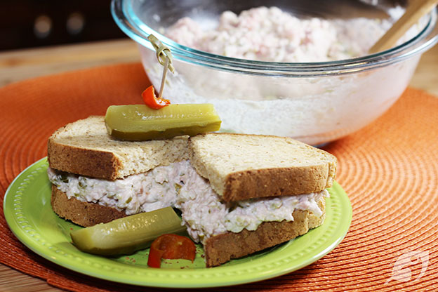 Ham Salad Sandwich on a plate with a pickle and the bowl of the spread in the background.