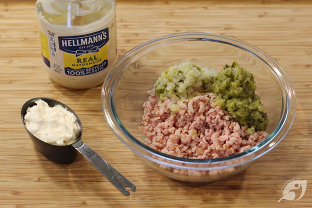 Ham, pickles, and onion ground in a bowl. Jar mayonnaise and 1/2 cup measure of mayonnaise in measuring cup.