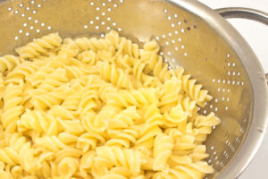 Fusilli pasta cooked al-dente’ draining in a colander. When cooked, drain the pasta, then rinse in cold water to bring the temperature down quickly, stopping the cooking process and keeping the noodles loose for the salad. Once cooled, transfer the cooled pasta to a colander or mesh strainer, shake to remove as much excess water as possible. Set aside for about 3 minutes to drain any additional water trapped.