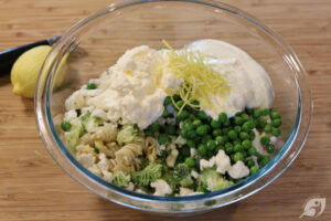 When thoroughly drained, place the pasta in a large bowl, add the broccoli, cauliflower, peas, prepared ranch dressing, mayonnaise, and lemon zest.