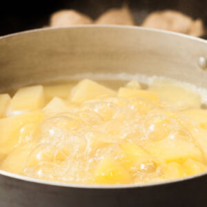 Cut the potatoes into uniform chunks and place them in a heavy saucepan along with the garlic. Cover with water, bring to a boil, lower heat to medium, and cook until the potatoes are fork-tender for about 20 minutes. [2]