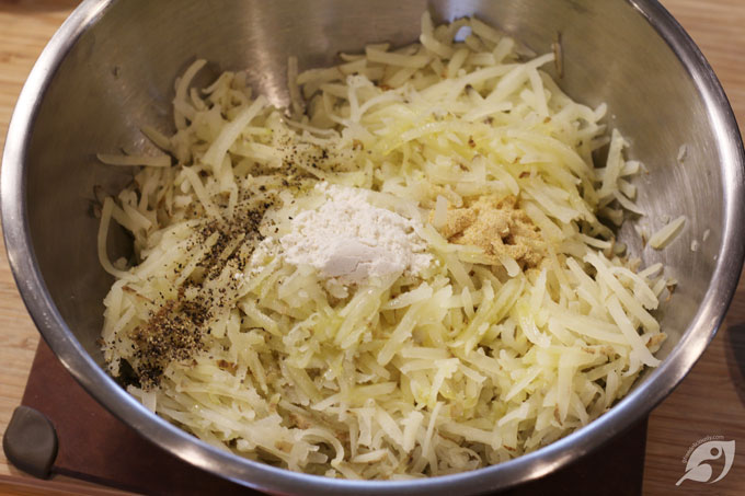 Once cooled, grate the potatoes into a large bowl. Add the grapeseed oil, flour, salt, garlic powder, and black pepper. Using your hands, gently fluff and turn the ingredients into the potatoes until evenly distributed.