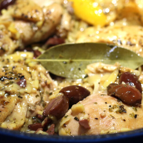 A beautifully captured image of a plate filled with vibrant and aromatic Chicken & Orzo with Lemon & Olives, accompanied by a yellow lemon slice and a few olive pieces.