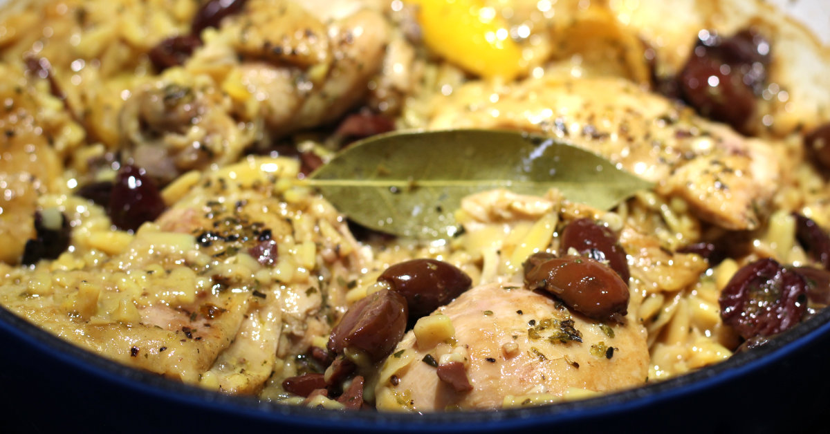 A beautifully captured image of a plate filled with vibrant and aromatic Chicken & Orzo with Lemon & Olives, accompanied by a yellow lemon slice and a few olive pieces.