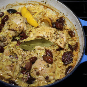 A beautifully captured image of a plate filled with vibrant and aromatic Chicken & Orzo with Lemon & Olives, accompanied by a yellow lemon slice and a few olive pieces.