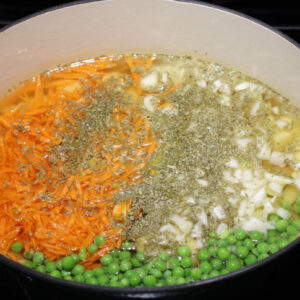 A large Dutch Oven is pictured, showing the combination of the starch (potatoes), base veggies, and aromatics with enough broth/liquid to cover the vegetables.