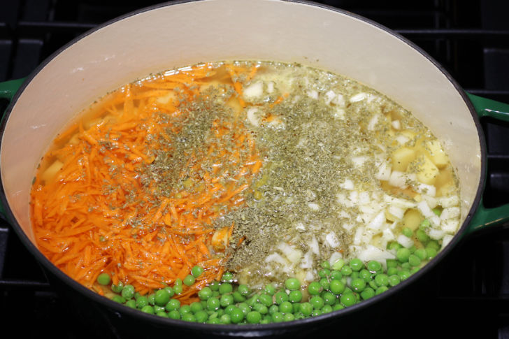 A large Dutch Oven is pictured, showing the combination of the starch (potatoes), base veggies, and aromatics with enough broth/liquid to cover the vegetables.