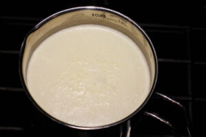 A pot is shown with 6 cups of scalded milk heated to 180°F until tiny bubbles form around the edges of the pan.