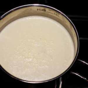 A pot is shown with 6 cups of scalded milk heated to 180°F until tiny bubbles form around the edges of the pan.