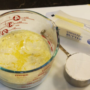 Photo shows 1 ½ cups of the scalded milk ladeled into a large glass measuring cup. The unsalted butter is adde to the cup with the milk to melt.