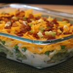 Styled photo showing a clear dish arranged on a green placemat with seven-layer salad in it.
