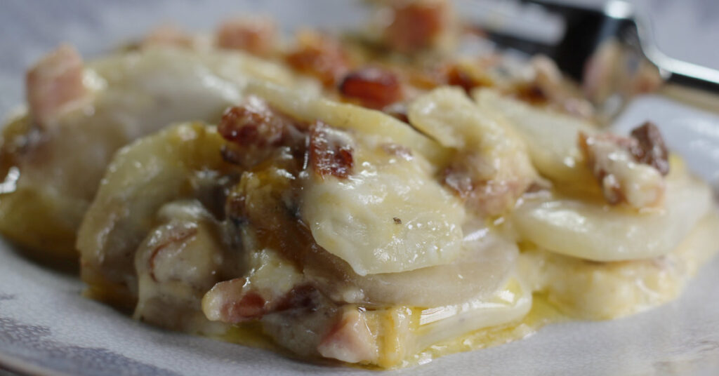 Closeup photo of Cheesy Scalloped Potatoes with Ham and Mushrooms with a fork in the background